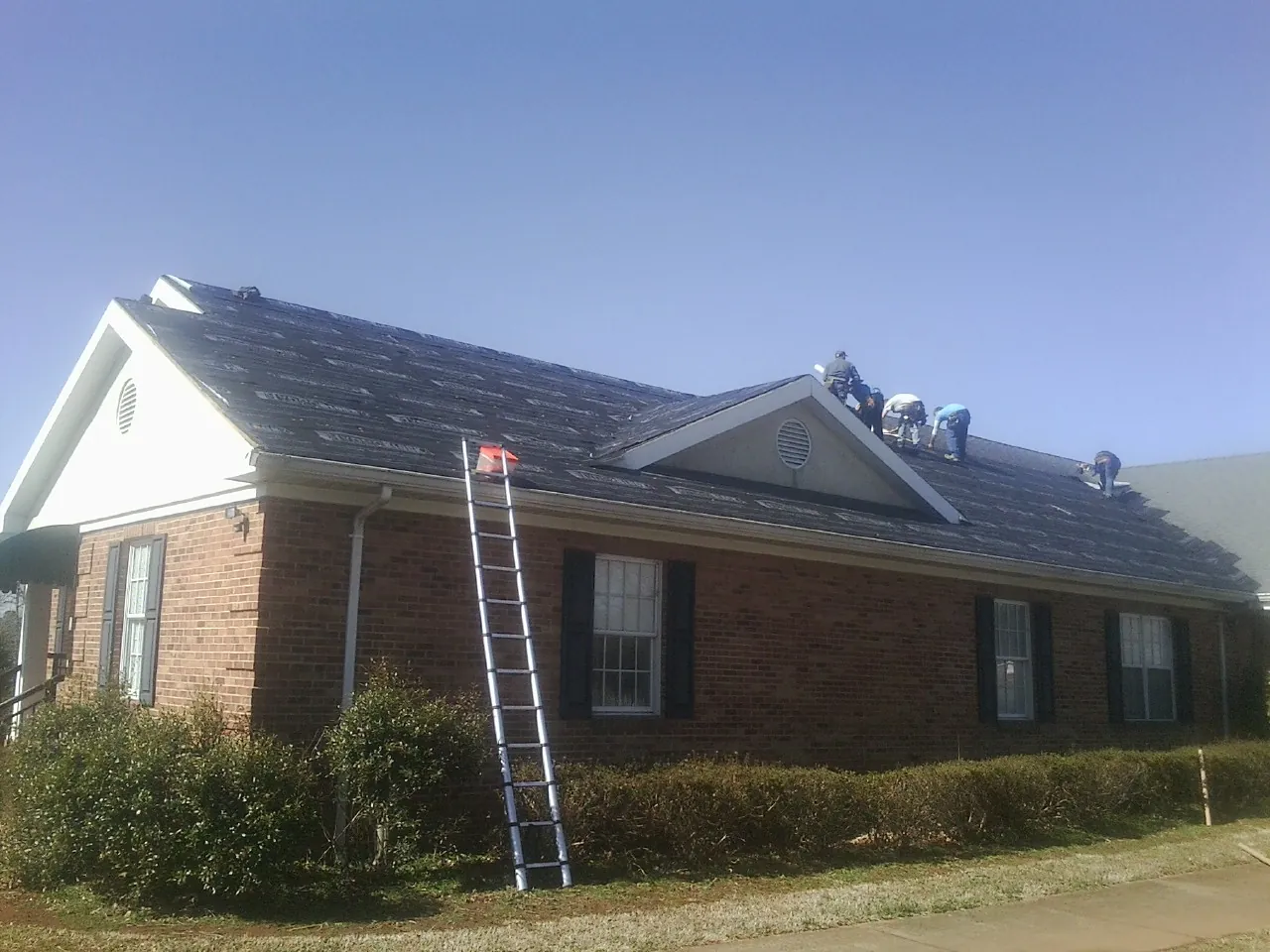 Crew tearing shingles off a brick ranch roof with a ladder set — Metal Roof Repair work by our crew in Roseboro