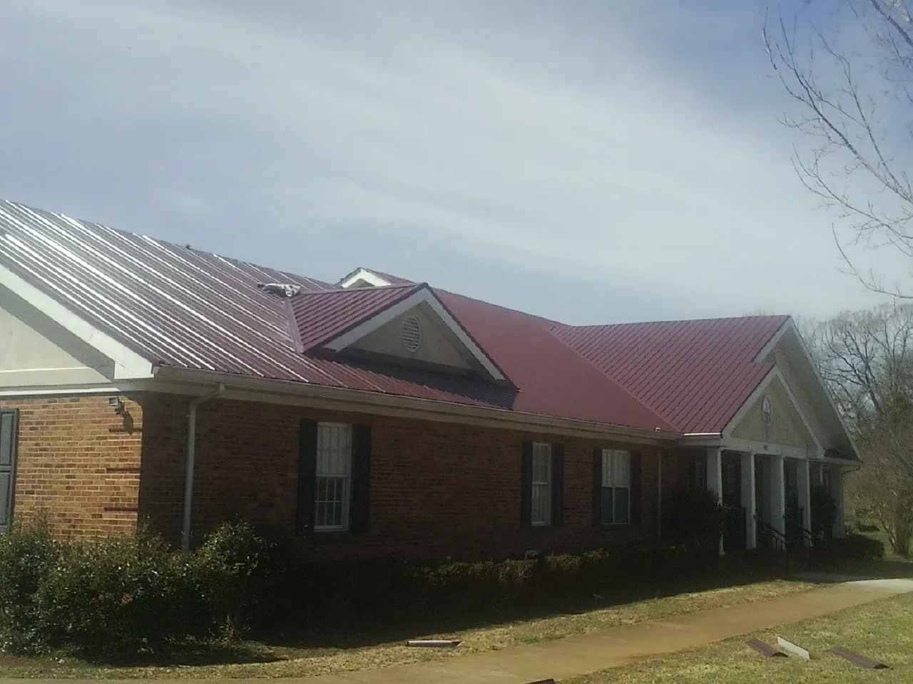 Red metal roof with gabled entries on a long brick building, from a Hail Damage Roof Repair job in Roseboro