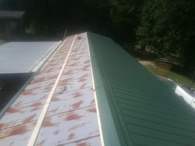 Old rusted panels beside newly installed green metal roofing — Wind Damage Roof Repair by Roofing Brothers in Roseboro