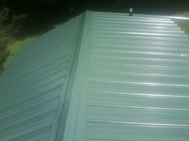 New green metal panels meeting at the ridge of a roof — Flat Roof Repair work by our crew in Roseboro