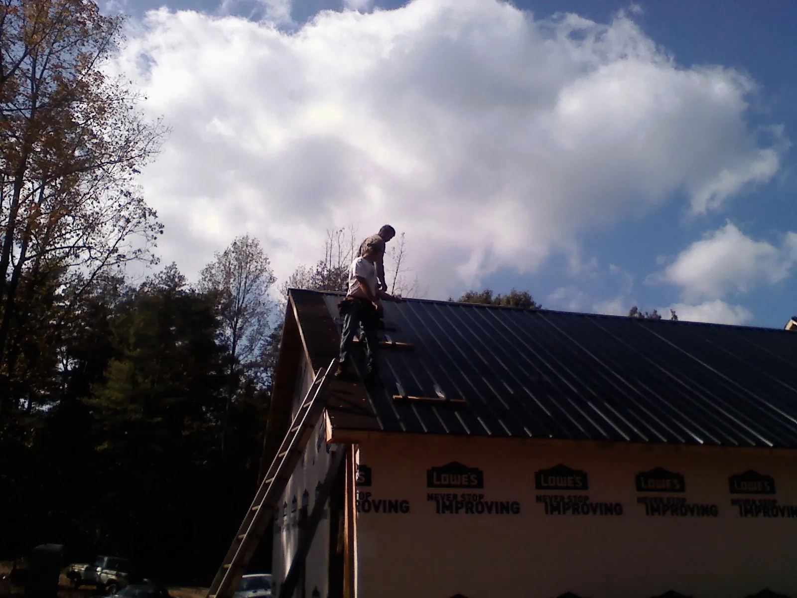 Roofer fastening dark metal panels high against a cloudy sky, from a Roof Inspection job in Roseboro