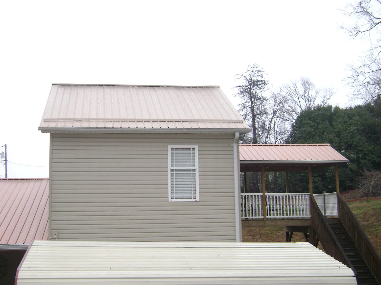 Tan metal roofs on a two story addition and attached porch, from a Roof Replacement job in Roseboro